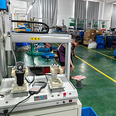 Factory worker using a dual action polisher in a well-equipped workshop, surrounded by various tools and machinery for car detailing.