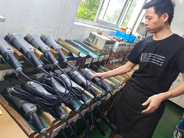 Man examining a variety of car polishers, including dual action and rotary models, displayed on a shelf in a workshop setting