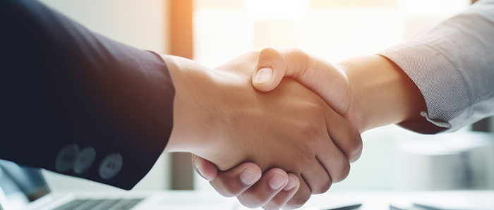 Business professionals shaking hands in a bright office, symbolizing a successful partnership in the car care industry, featuring tools like car polishers and buffers.